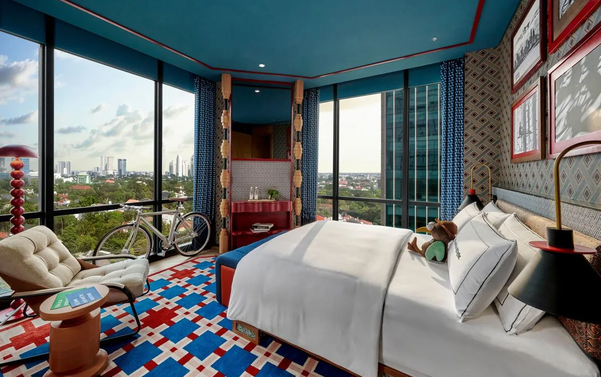 Reference image: a high-rise hotel bedroom with patterned walls, a blue and red checked carpet and a city view.
